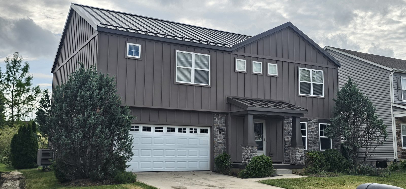 Two-story home finished in dark brown Battenlok board and batten steel siding with stone accent